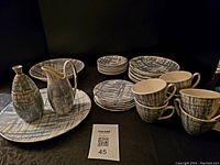 Full set of Blue Dell by KilnCraft USA mid-century modern dinnerware including plates, bowls, cups, creamer, and covered sugar bowl arranged on black surface.