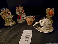 Full lot photo showing porcelain figurines of clown couple, dancing couple, ceramic pitcher, sauce boat, and one bird lamp base.