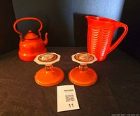 Photo of orange porcelain on steel kettle, plastic jug, and glass candlesticks on black background