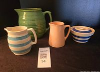 Four vintage pottery items including three jugs and one lidded bowl shown together on dark background.