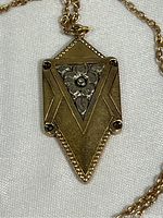 Close-up image of the gold tone pendant featuring geometric and floral designs on a white fabric background, showing detail on the front of the pendant.