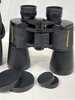 Close-up image of Bushnell binoculars with front and rear lens caps removed, showing the lenses and Bushnell branding.