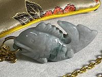 Close-up of the carved stone fish pendant hanging from a gold tone chain, showing detailed scale and fin carvings.