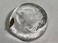 Overall view of the clear round crystal paperweight showing the bird in branch design and original sticker on the side.