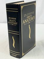 Front angled view showing the black hardcover of Gray's Anatomy with gold lettering and spine details including the text 'The Unabridged Gray's Anatomy' and a vertebral column illustration.