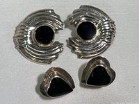 Top view of four earrings, two large round with ridged silver and two smaller heart-shaped with smooth silver and black stones.