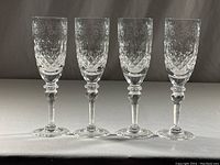 Four clear crystal champagne flutes with floral and diamond-cut patterns, lined up