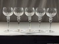 Five crystal wine glasses lined up on a flat surface, showing uniform size and design