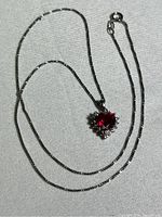 Full view of the sterling silver chain and attached red heart pendant lying on fabric.