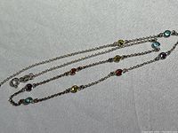 Close-up image of the delicate sterling silver chain necklace with multiple evenly spaced faceted crystal stones in various colors on a light background.