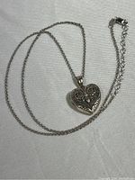 Heart-shaped sterling silver locket on chain, showing full chain and locket in flat arrangement on fabric.