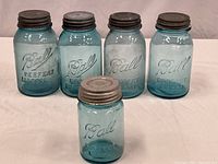 Five blue Ball Perfect Mason jars with metal screw-on lids, four taller (7-inch) and one shorter (5.5-inch), arranged on white surface.