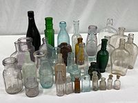Full view of 29 vintage bottles arranged on white surface showcasing color and shape variety