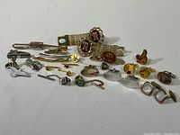 Overview of the vintage men's accessories collection showing multiple tie clips, cufflinks, pins, and a watch band on white background.