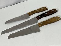 Three vintage kitchen knives laid out side by side with wooden handles and stainless steel blades showing usage wear.