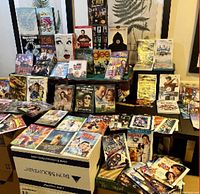 Wide view of various DVDs arranged on tables and boxes, showing titles and collections of family and children movies, series, and boxed sets.