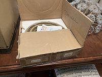 Photo of open cardboard box showing the new ceiling light fixture with three gold metal rings and bulb sockets inside.