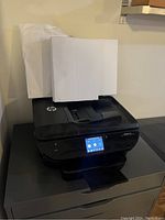 Front angle photo of black HP Envy 7640 printer loaded with paper in tray.