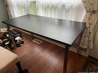 Full view of black rectangular desk with angled legs placed by window on wooden floor