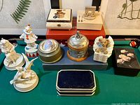 Full layout of the various music and jewelry boxes on a green felt surface showing different figurines and box styles.