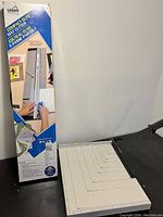 Boxed Logan Compact Elite Mat Cutter on left and the mat cutter on the right with a grid base.