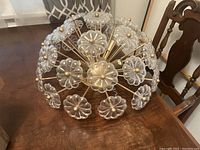 Spherical sputnik-style ceiling lighting fixture with a gold metal frame and clear glass flower-shaped elements with gold centers, placed on a wooden table.