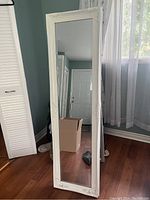 Full-length white framed standing mirror upright on floor near window showing entire mirror and frame.