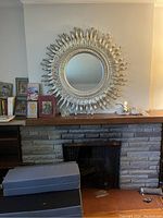 Full view of the sunburst decorative mirror hanging above a stone fireplace mantel showing the overall condition and setting.
