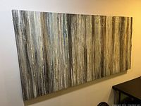 Front view of large rectangular abstract art canvas on wall showing textured vertical stripes in gray, beige, and gold tones.
