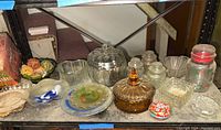 Shelf showing amber glass jar with lid, clear pumpkin-shaped jar, small glass containers, and various decorative glass dishes.