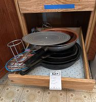 Drawer containing four cast iron frying pans stacked and two metal beer can chicken holders visible.