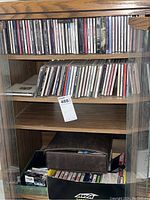 Full shelving unit with two shelves of assorted CDs and lower shelf with boxes containing cassette tapes and other music media.
