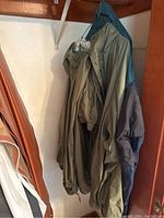Multiple men's jackets hanging on a rod inside a closet, several in neutral colors including olive green and navy.