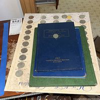 Overall view of coin folders, handbook, and vintage coin album page displayed on a table