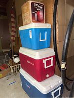 Stacked photo of three Coleman coolers in blue, red, and navy blue with white lids, showing the Tip n Tap jug box on top.