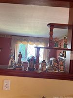 Wide view of nine figurines on wood shelving including various Goebel, Llardo, Willow Tree, and vintage figurines