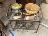 The lot items displayed on a metal cart including mixing bowls, strainers, and Pampered Chef kitchen utensils in packaging.