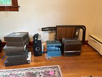 Lot photo showing Bell and Howell projector, film reels and slides, Commpco projector table, and multiple boxes of slides or reels arranged on floor.