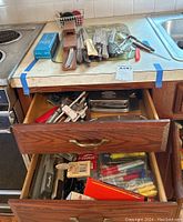 View of an open drawer containing various kitchen knives and utensils alongside a top counter with knives and other kitchen tools laid out