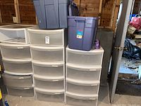 Multiple white plastic storage drawer units with translucent drawers and several large purple plastic storage bins stacked on top.
