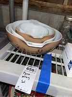 Four nesting Pyrex Americana mixing bowls with peach exterior and black Americana motif, shown stacked on a shelf with tag indicating 'Pyrex Mixing Set'.