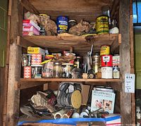 Wide view of three wooden shelves containing assorted nuts, bolts, fasteners, painting supplies, sanders, and tools inside a cabinet.