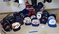 Overview of various New England Patriots, Red Sox, and Athletics baseball caps and winter hats arranged on floor