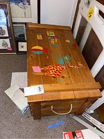 Top and side view of wooden toy chest with painted animal designs on lid and rope handles on sides.