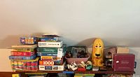 Shelf with assorted puzzles, colorful block sets, figurines, and a large yellow character toy.