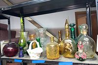 Photo showing a variety of colored glass bottles and vases in different shapes and sizes on a shelf.