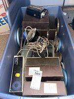 Stored film reels in original brown and blue cases and a metal light with cord inside a plastic bin.
