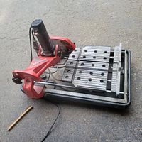Full view of the Husky portable wet tile saw showing the red frame, metal cutting table with holes, and attached water tray underneath.