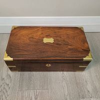 Top view showing rich rosewood grain pattern with brass corner covers and central brass inlay on lid
