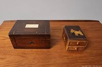 Two antique wooden boxes on a wooden surface, one larger with keyhole and inlay, the other smaller with drawers and animal motifs.
